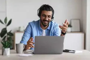 Mann mit hellblauem Hemd sitzt im HomeOffice vor einem Laptop und spricht beim Live Online Seminar für Firmen mit der fingerLINK-Trainerin.
